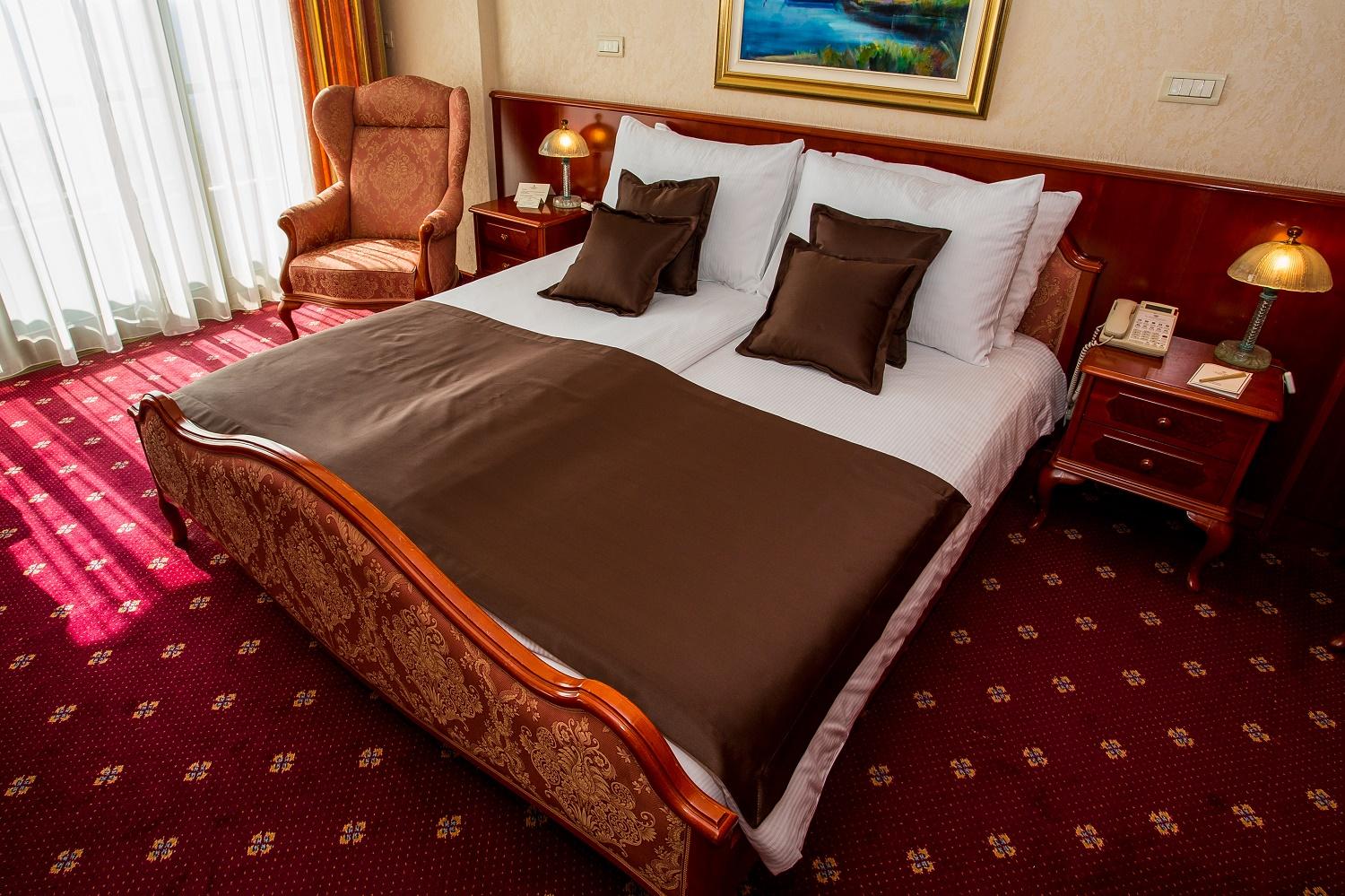 Grand Hotel Bernardin Portoroz Exterior photo The photo shows a well-decorated bedroom featuring a large bed with a light-colored headboard and neatly arranged white linens. The bed is adorned with a brown bedspread and decorative pillows. On either side of the bed, there are wooden nightstands 