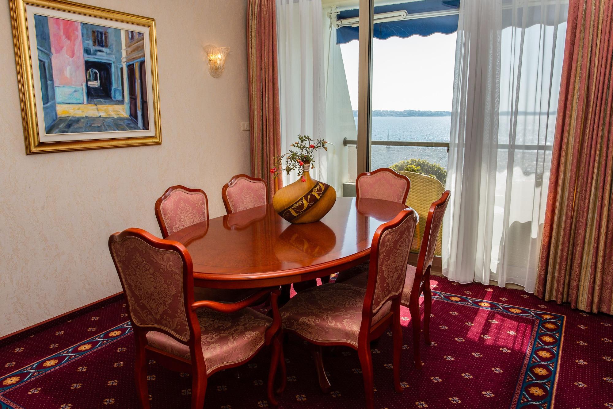 Grand Hotel Bernardin Portoroz Exterior photo The photo shows an elegant dining area with a wooden round table surrounded by six upholstered chairs. The chairs have a decorative pattern and are positioned around the table. A small vase with flowers sits at the center of the table. In the backgro