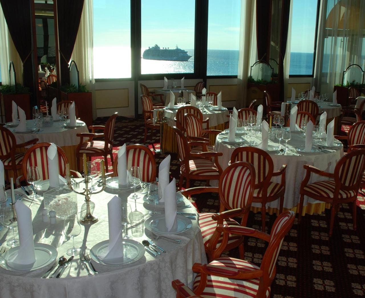 Grand Hotel Bernardin Portoroz Exterior photo The photo shows an elegant dining area with several round tables adorned with white tablecloths. Each table is set with dishes, cutlery, and folded white napkins. The decor features wooden chairs with a striped pattern. Large windows provide a view o