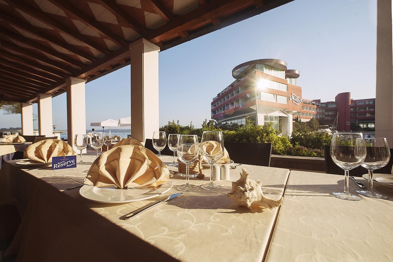 Grand Hotel Bernardin Portoroz Exterior photo The photo depicts a dining setup at a restaurant, featuring elegantly arranged tables on a terrace. Each table is covered with a light-colored tablecloth and has an artistic napkin folding resembling a flower. There are several empty wine glasses and