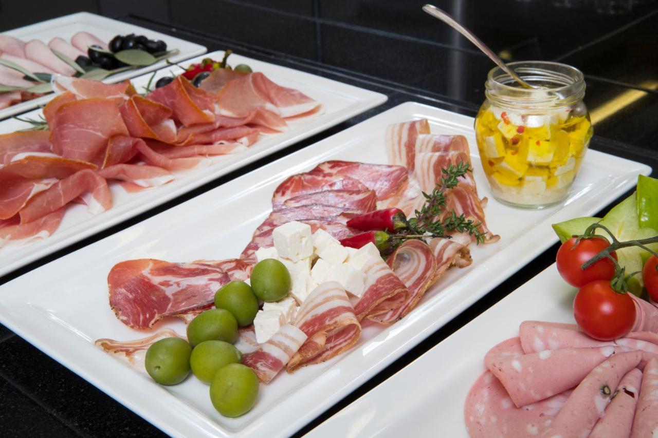 Grand Hotel Bernardin Portoroz Exterior photo The photo shows a selection of charcuterie and accompaniments arranged on white plates. There are various types of cured meats, including slices of ham and salami, presented attractively. In the center, there are green olives and pieces of cheese, al